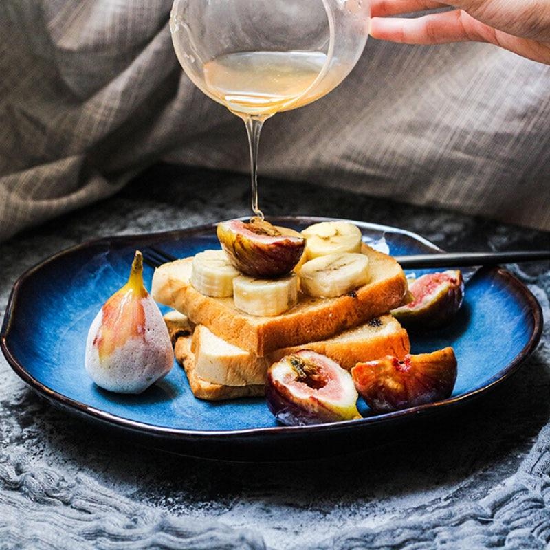 Taygete Plate with solid round ceramic design featuring bread, figs, bananas, and honey drizzled on top.