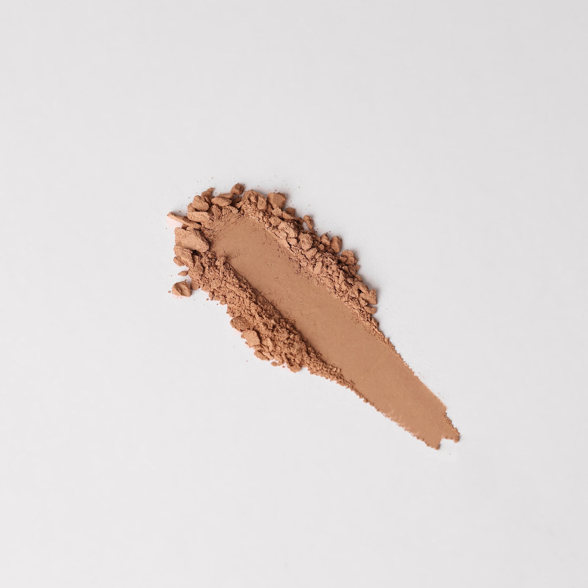 Close-up of vegan pressed Face Powder swatch showing smooth texture and light brown color on a white background.