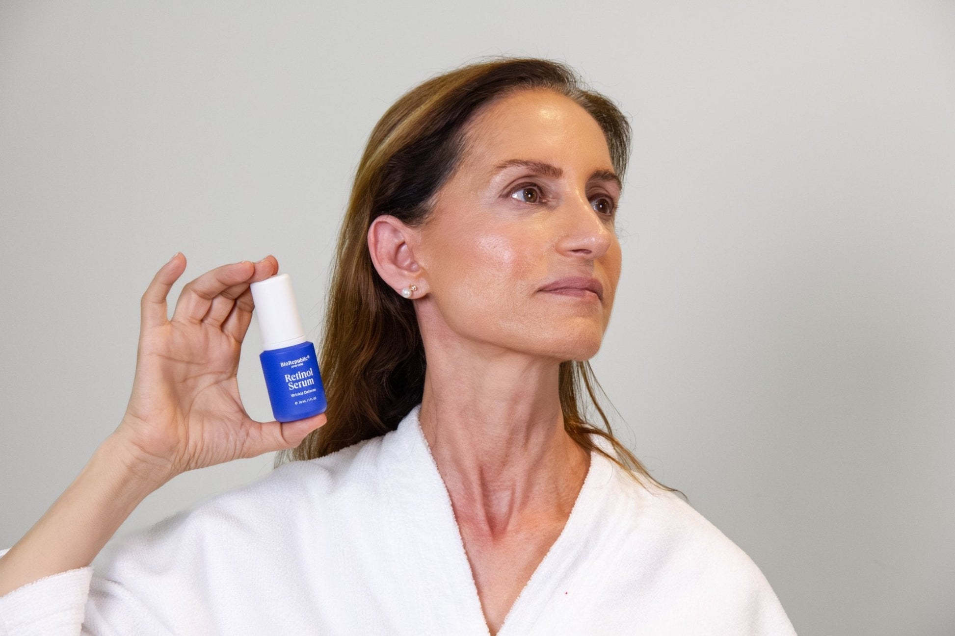 Woman holding Retinol Wrinkle Defense Serum bottle, showcasing its use for smoothing fine lines and wrinkles.