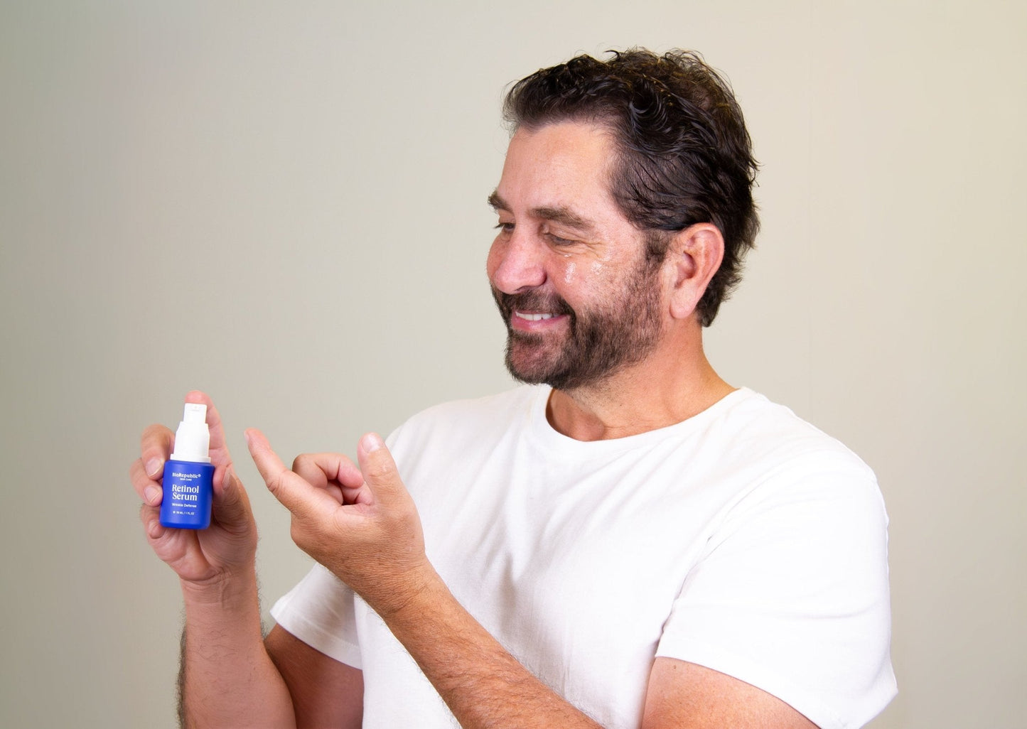 Man smiling and applying Retinol Wrinkle Defense Serum, a powerful anti-aging skincare product, to his hand for smooth skin results.