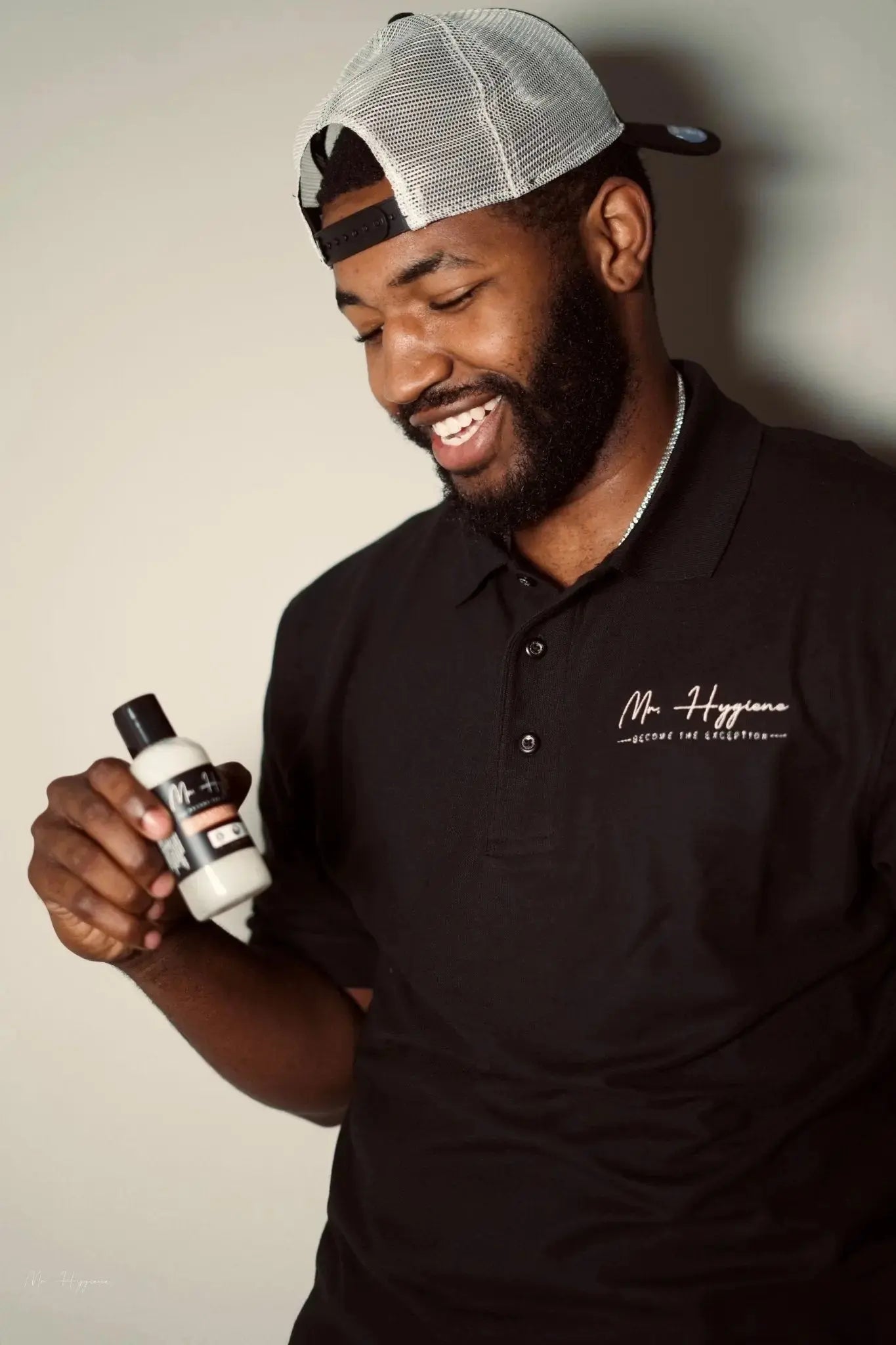 Smiling man holding Sandalwood Beard Wash & Conditioner in black polo and cap