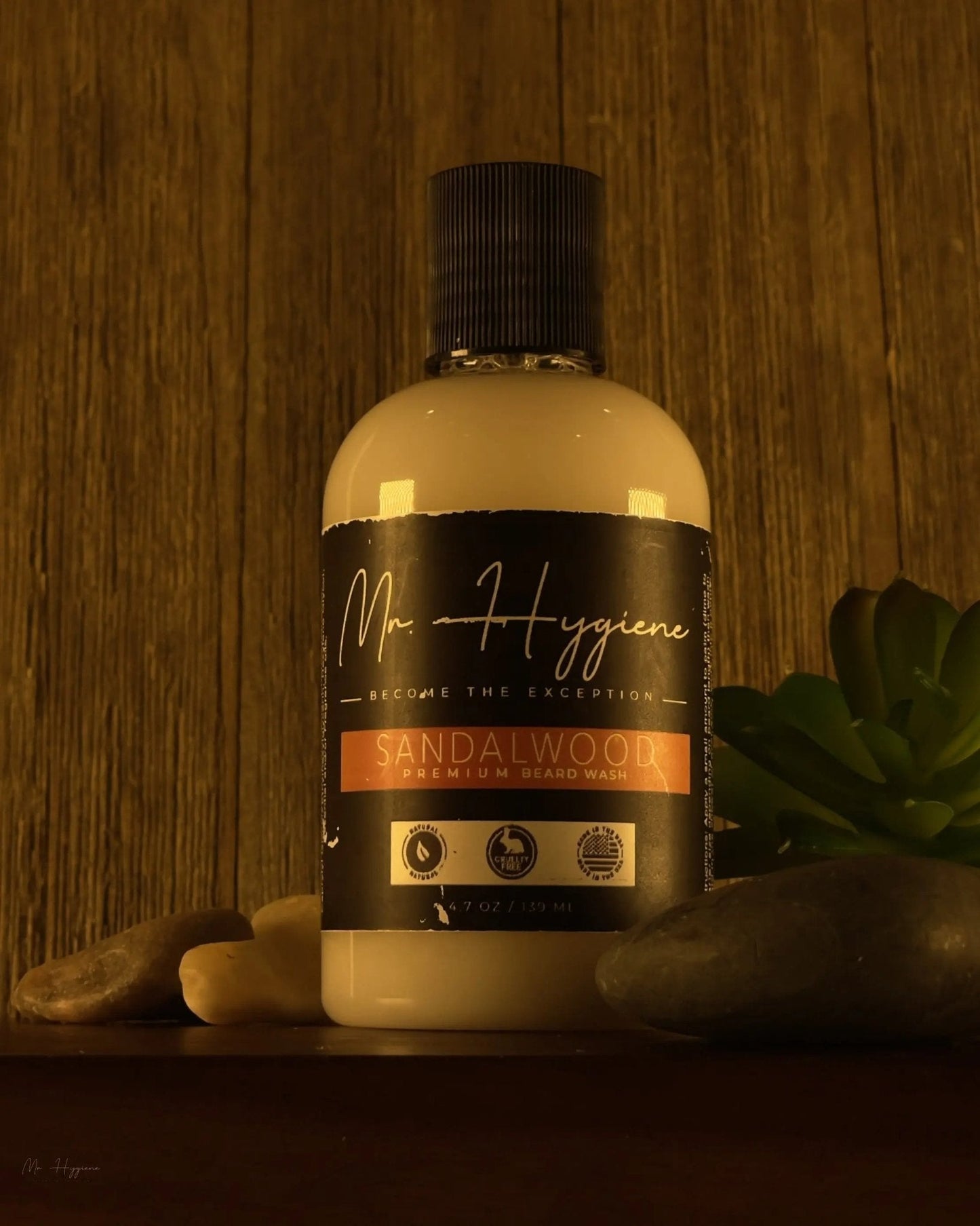 Sandalwood Beard Wash & Conditioner bottle on wooden background with rocks and plant decor.