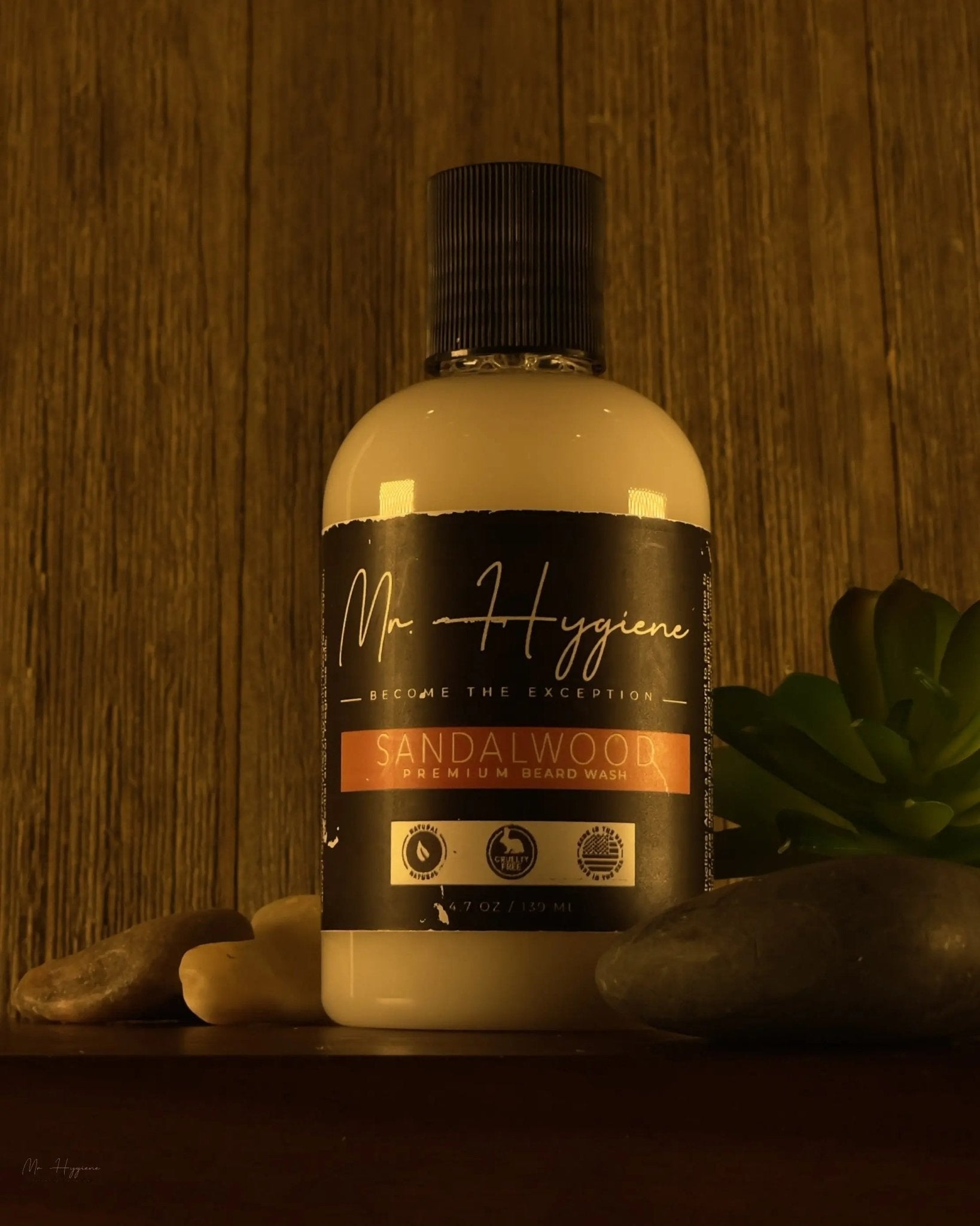 Sandalwood Beard Wash & Conditioner bottle on wooden background with rocks and plant decor.