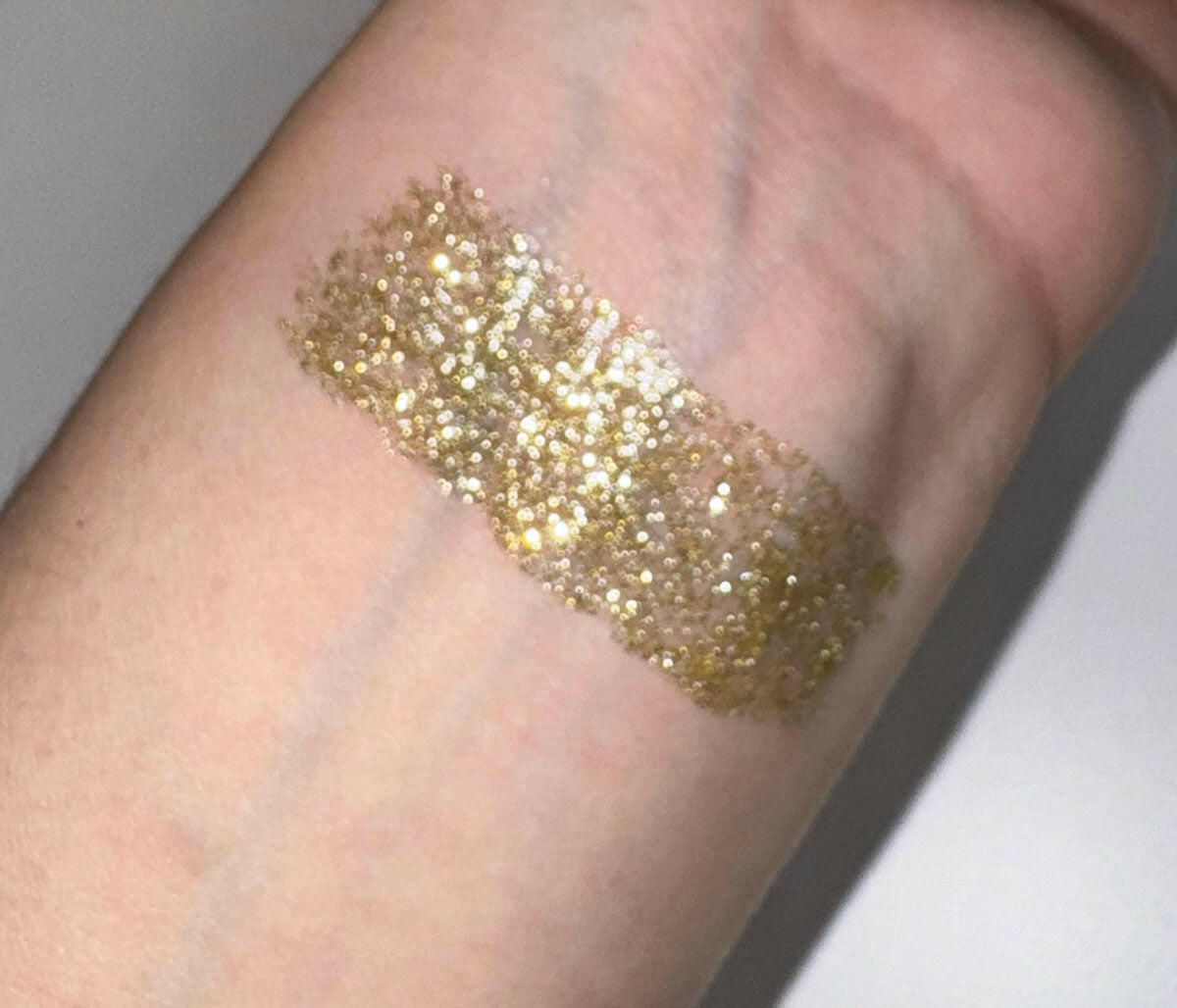 Swatch of Stardust - Flicker Glitter Eyeliner in white gold glitter shade on skin.