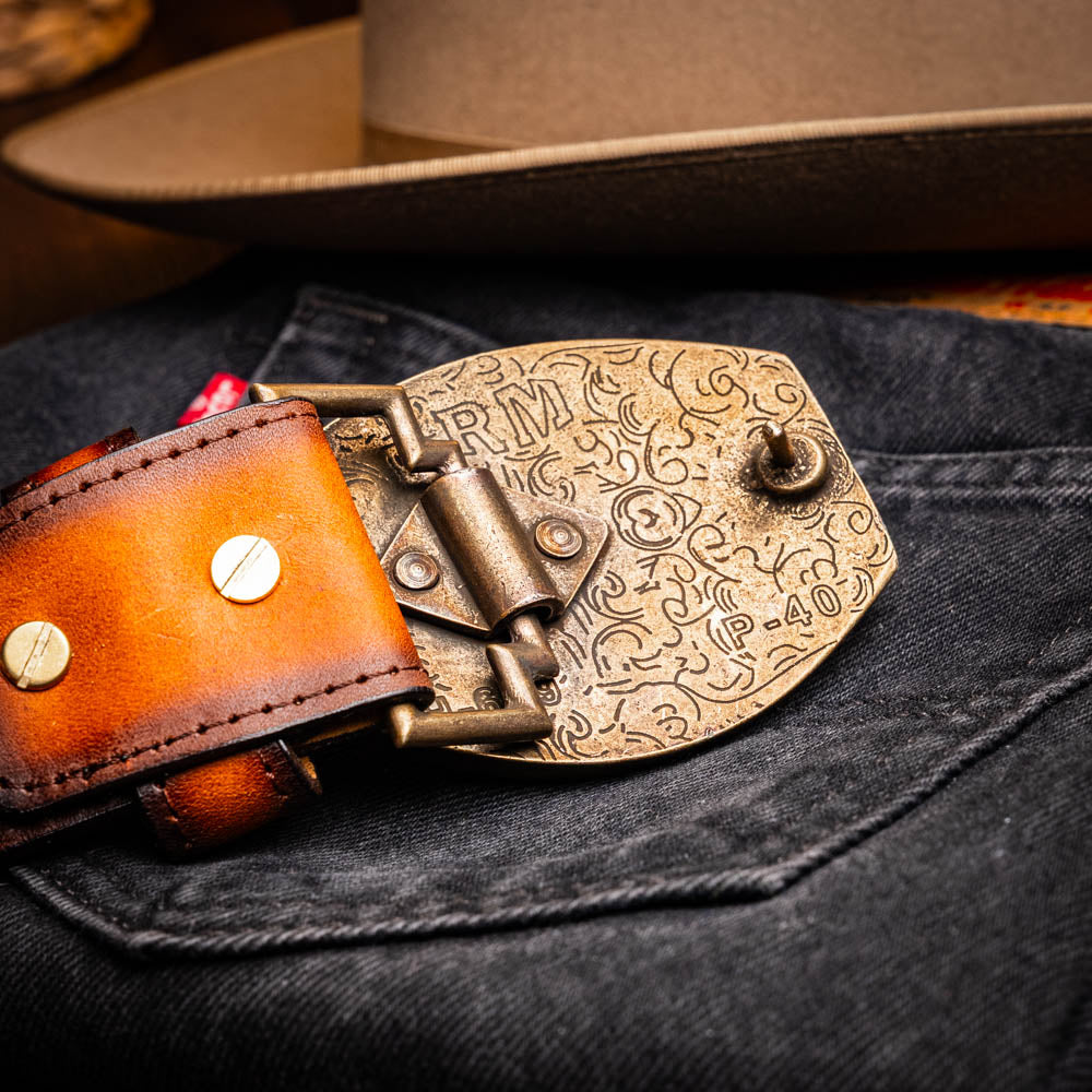 Texas Belt Aged Brown with intricate brass buckle and cowboy hat background