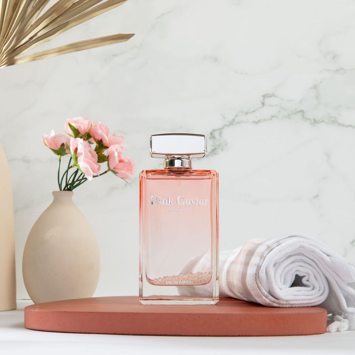 Elegant Syren - Pink Caviar fragrance bottle on marble, surrounded by flowers, conveying luxury and feminine elegance.