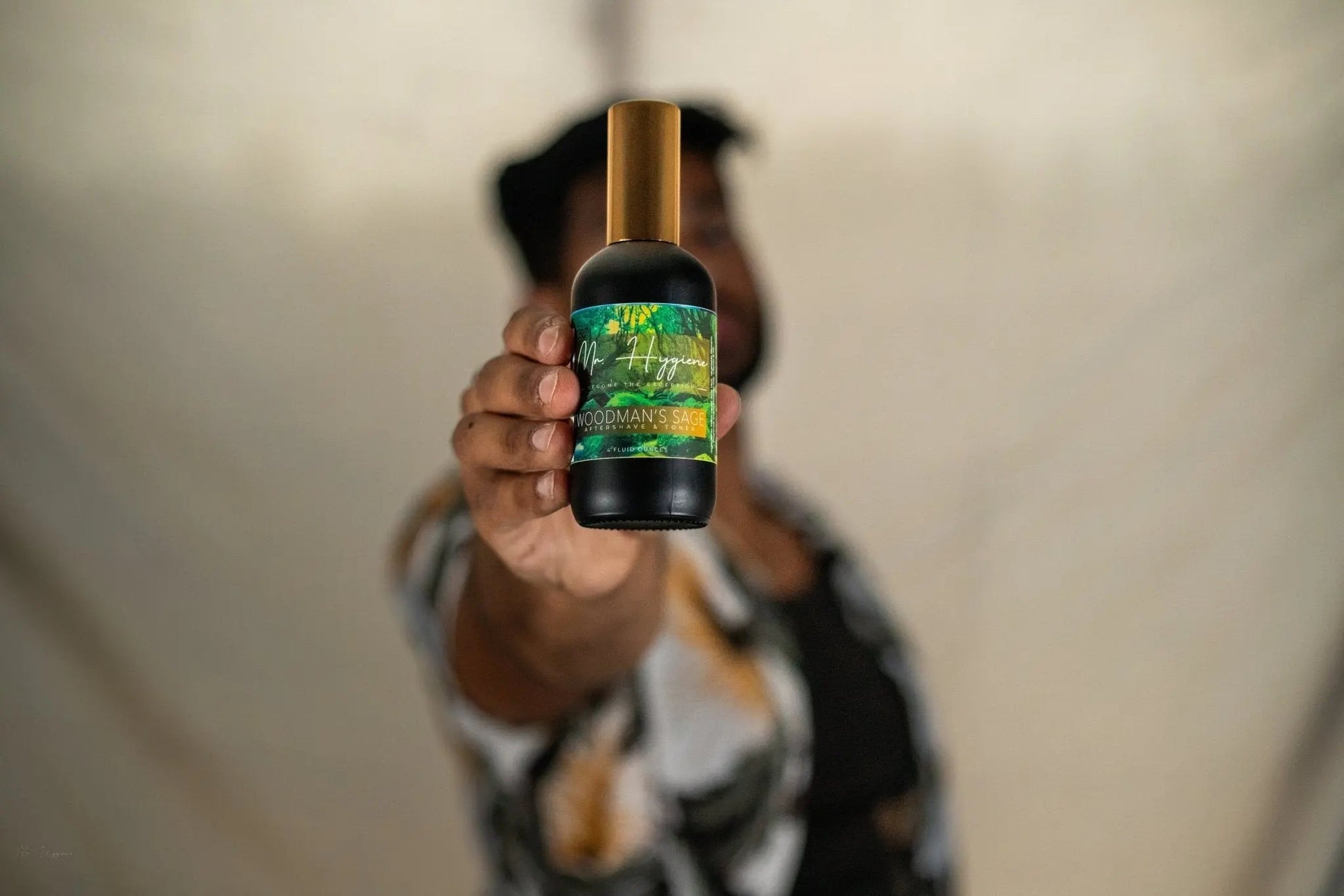 Person holding a bottle of Woodman's Sage Mens Aftershave & Toner with green and gold label, ideal for soothing post-shave skin.